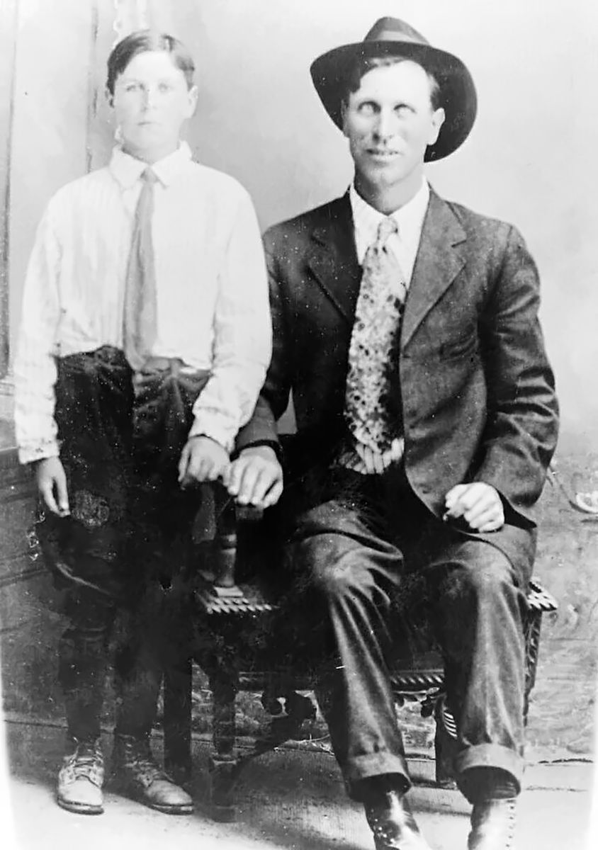 A studio portrait: a seated young man in a sack suit, patterned tie and wide-brimmed hat, with a boy of about twelve in a white shirt standing beside him with a hand on the chair.